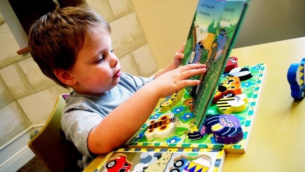 Robby Rathel, 3, flips through a children’s book after finishing a puzzle.